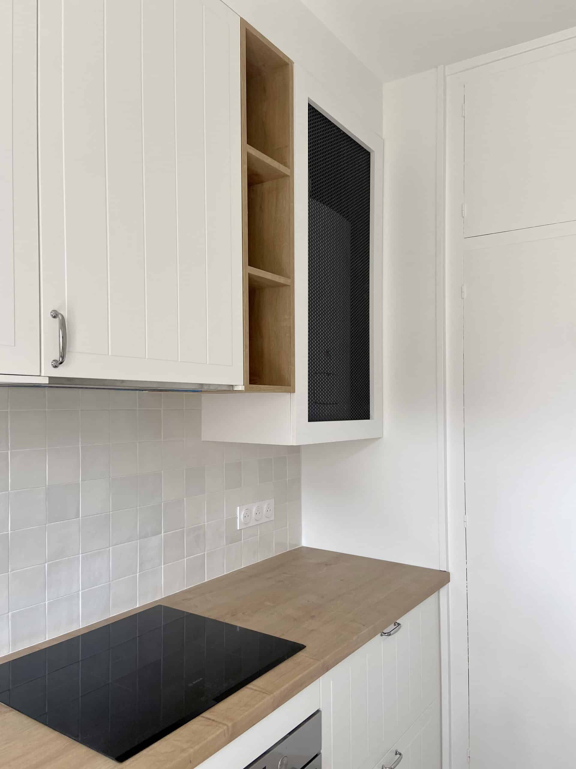 Cuisine moderne blanche et bois clair avec plaque à induction noire, carrelage mural clair et prises électriques françaises. Armoires à portes à panneaux.
